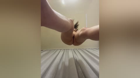 A video of two people from a low-angle view, focusing on their thighs and genitals, with light beige walls and a gray curtain in the background.