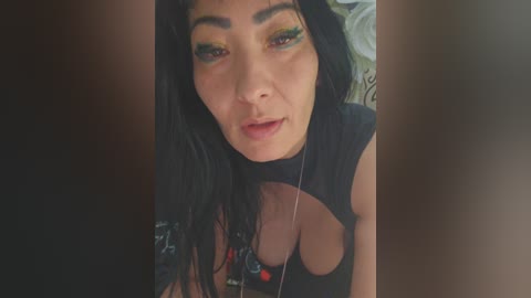 Video of a young woman with long black hair, wearing a black top with cutouts, showcasing a curvaceous figure and large breasts, with bright yellow eyeshadow.