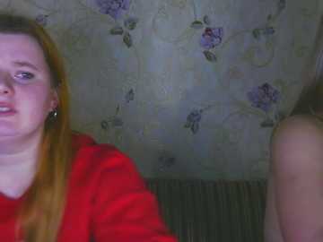 Video of a young woman with long red hair, wearing a red sweater, smiling, against a floral-patterned wallpaper background.