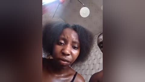 Video of an African-American woman with a large afro, wearing a black tank top, looking upset or frustrated, with a showerhead in the background.