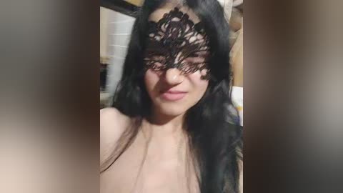 Video of a smiling Asian woman with long black hair, wearing a black lace mask, standing indoors against a blurred kitchen background.