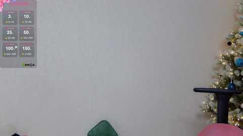 A video of a minimalist living room with a plain white wall, a digital fitness tracker displaying workout stats, a green armchair, and a decorated Christmas tree in the background.