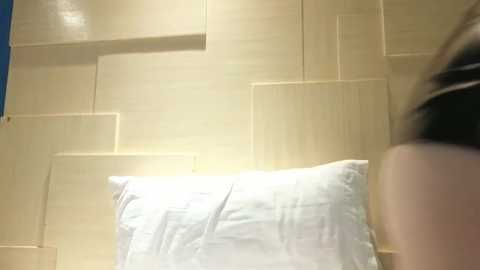 Video of a person's back with a white pillow on a beige wood-paneled wall, blurred head, suggesting movement.