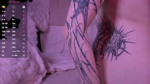 Video of a pale-skinned person with extensive black ink tattoos, including a large shark on the chest, in a dimly lit room with soft pink lighting.
