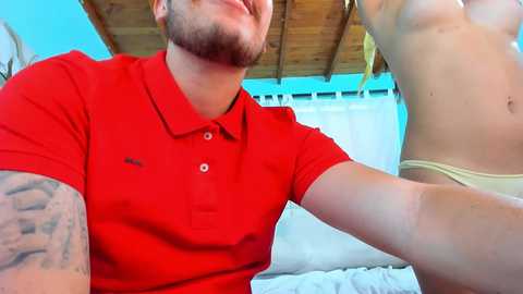 A close-up video shows a bearded man in a red polo shirt, tattoos on his arm, taking a selfie with a partially visible woman in a yellow bikini.