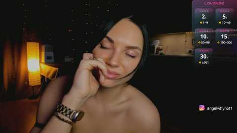 Video of a light-skinned woman with long black hair, wearing a gold wristwatch, talking on a phone, set in a dimly lit room with a glowing lamp and digital live stream overlay.