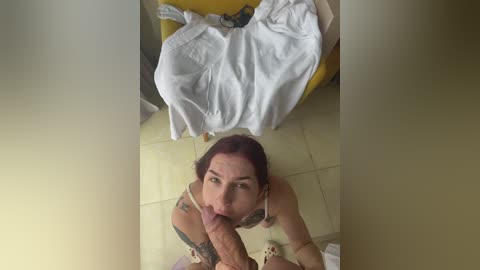 Video of a woman with red hair, wearing a white dress, kneeling on a tiled floor, performing oral sex on a man with a circumcised penis.
