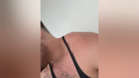Video of a close-up of a person's bare shoulder and neck with visible tattoos, wearing a black tank top, partially obscured by another person's arm.