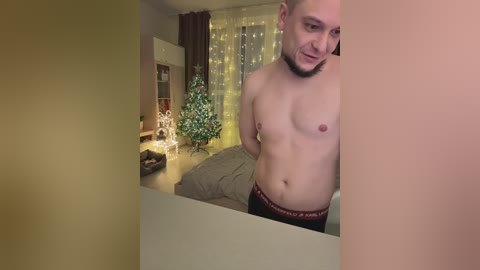 Video of a shirtless, bearded man in black Calvin Klein underwear, standing in a cozy, warmly-lit bedroom with Christmas decorations.