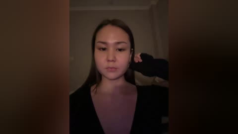 A dimly lit video of a young woman with fair skin, straight brown hair, and a black dress, being pulled by an unseen person's hand. The background is blurred, suggesting an indoor setting.