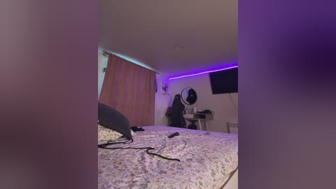 Video of a dimly lit bedroom with a large bed covered in a floral-patterned duvet, purple LED strip lighting, and a person wearing a black mask standing near a desk with a computer monitor and keyboard.