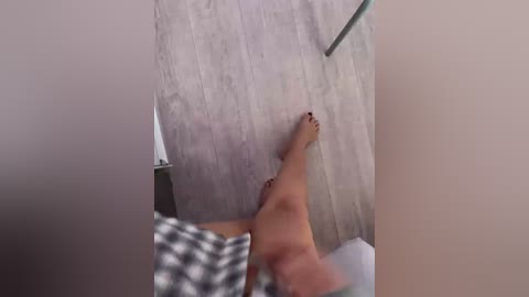 Video of a light-skinned woman's bare legs, painted toenails, lying on a checkered blanket, with a textured wall in the background.