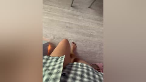 Video of a person with fair skin and red toenails lying on a light gray, textured wooden floor. The image is slightly blurred and taken from a low angle.