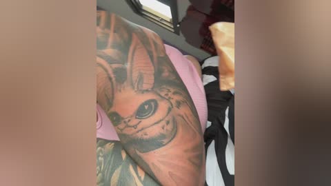 Video of a person's arm with a large, realistic tattoo of a smiling cartoon fox on the upper forearm, visible against a white bedsheet and a pink pillow. The background includes a window and a partially visible person's leg.