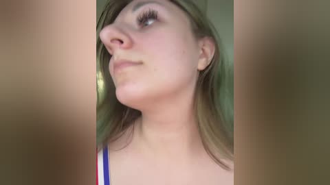 A close-up video of a young Caucasian woman with light skin, straight shoulder-length brown hair, and a neutral expression. She wears a sleeveless top with thin straps. The background is blurred.