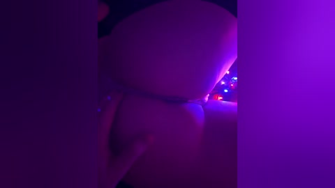 A dimly lit video captures a close-up view of a woman's buttocks, partially covered by a black thong, under purple lighting.