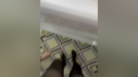 Video of a close-up, blurred view of a patterned textile with green and beige diamond shapes, likely a blanket or fabric, set against a soft, muted background.