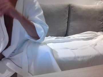 Video of a person in a white hospital gown, lying on a gray couch, with blurred background.