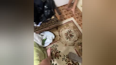 A video of a messy living room floor with a patterned rug, scattered clothes, and a black backpack. The image is blurry with a brown and beige color palette.