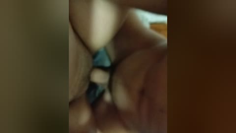 A blurry video featuring a close-up of a person's hand, possibly engaged in a sexual act, with a dark-colored object between their fingers. The background is indistinct and out of focus.