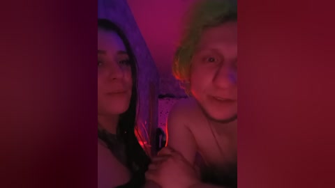 A video of two women with dark hair and light skin, one in a red dress and the other in a yellow top, in a dimly lit room, smiling.