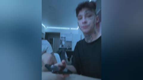 A video of a young, pale-skinned, short-haired boy with a slightly blurry face, playing a video game in a dimly lit, modern kitchen with blue LED lighting.