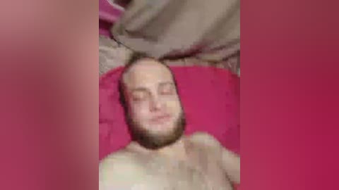 A video of a bearded man with closed eyes lying on a pink bedspread, with a blurry, pink-framed foreground.