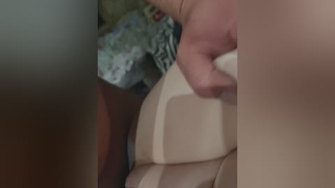 A close-up video shows a hand pressing against a beige cushion, partially visible, in a dimly lit room with a floral-patterned blanket in the background.