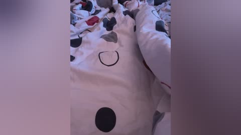 Video of a messy bedroom with a white bear plush toy and scattered clothing; bear has a black circle on its face, surrounded by a polka-dot pattern.