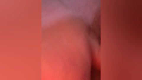 A blurred, close-up video of a person's bare buttocks against a gradient background transitioning from red to orange, with no discernible facial features or additional details visible.