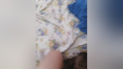 A blurry video of a hand touching a white floral-patterned fabric with blue and yellow hues. The background is indistinct, with a blue and black texture.
