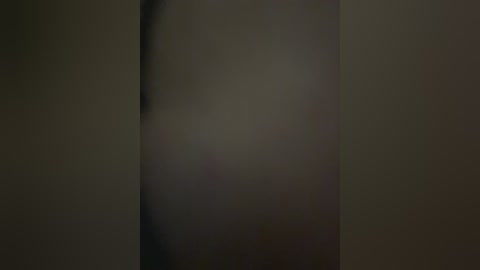 A dimly lit, blurred video of a person's upper body, with a focus on the chest and shoulders, showing indistinct skin tones and a hint of a dark object on the left side.