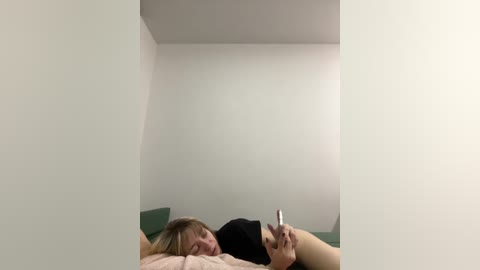 A video captures a blonde woman in a green top lying on a bed, holding a phone. The room has white walls and minimal decor, creating a minimalist, modern aesthetic.