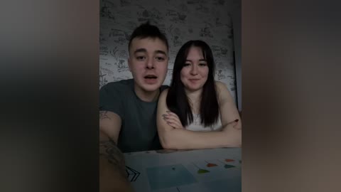 A video shows a young couple with tattoos; the man in a dark T-shirt, the woman in a white top. They are leaning over a colorful painting with fish and water, set against a wallpapered background.