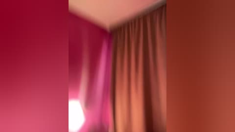 A video of a corner room with a pink wall, beige curtain, and an orange wall. The room's lighting creates a soft, warm ambiance.