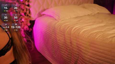 Video of a woman in a black bra lying on a bed with a beige quilt, surrounded by pink and purple ambient lighting.