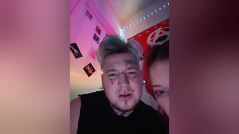 Video of a young, pale-skinned, bald man with a mohawk, wearing a black sleeveless shirt, covered in facial tattoos, and surrounded by neon lights and posters in a dimly lit room.