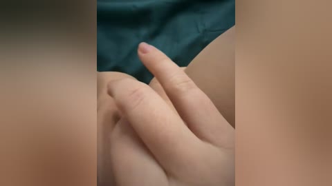 Video of a close-up view of a light-skinned hand with a small, erect penis between the fingers, lying on dark blue fabric, likely a bed sheet.