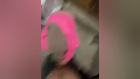 A blurred, low-resolution video depicts a person in a bright pink hooded sweatshirt, with indistinct facial features, against a pink and grey background. The image is unclear and lacks distinct details.