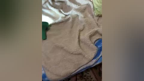 Video of a child in a cozy, beige fleece blanket with a blue and green striped pillow. The background includes a patterned rug and partially visible clothing. The image appears candid and intimate.