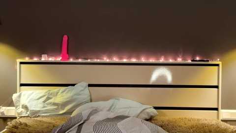 Video of a modern bedroom with a beige headboard, a pink dildo on the nightstand, and a white fur rug.