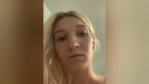 Video of a young, light-skinned, blonde woman with straight hair, looking serious. She's in a bathroom with beige walls and a mirror.