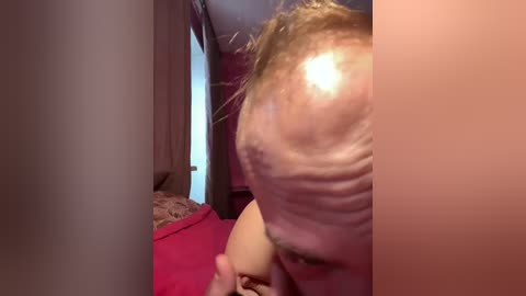 Video of a close-up of a person with a large, sagging belly, visible in profile, lying on a bed with red sheets and a beige blanket.