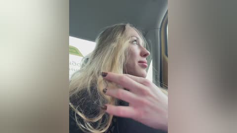 Video of a young woman with long blonde hair, light skin, and a contemplative expression, leaning against a car window, with a blurred cityscape background.