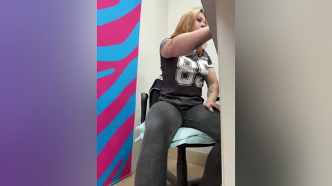 Video of a blonde woman in a grey \"Buffalo Bills\" jersey, sitting on a chair in a brightly colored room with blue and purple walls.