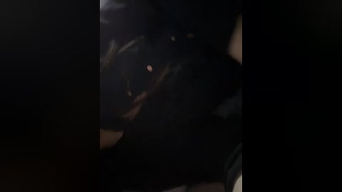 A dimly-lit video of a person wearing a black leather jacket and dark clothing, with a hint of red light in the background, creating a shadowy and mysterious atmosphere.