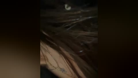 A close-up video of a human scalp with dark, tangled hair and a visible mole on the skin, set against a dimly lit, dark background.