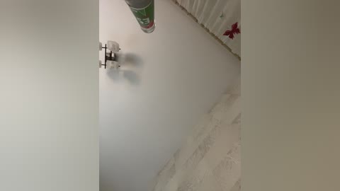 A video of a white wall with a large green and red can and a white curtain with lace.