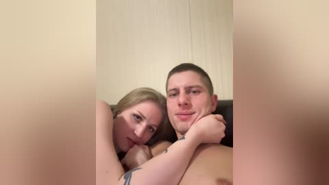 Video of a naked Caucasian couple, a blonde woman and a man with short brown hair, lying close together on a bed. Both have light skin tones.