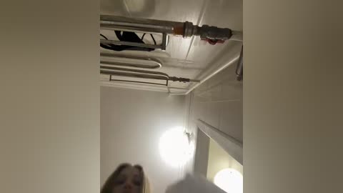 A video of a narrow, dimly lit corridor with white walls, a bright light at the end, and pipes running along the ceiling. A hand is visible in the foreground.